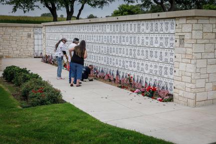 Four people mourning in front of a columbarium with American flags and flowers at the base.