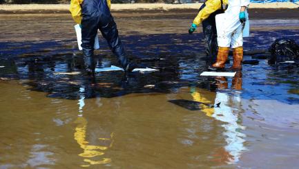 2 men wade in an oil spill in the ocean.