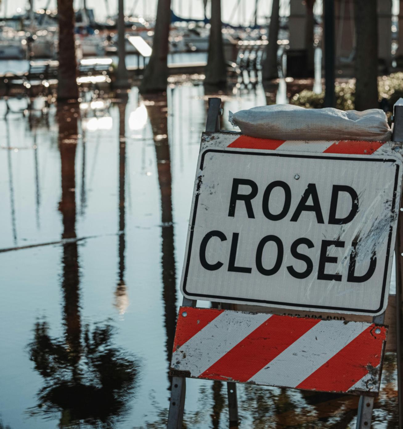 A flooded street with a road closed sign and sand bags.