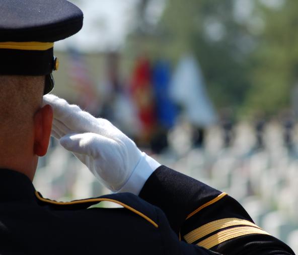 American soldier in full dress uniform saluting fallen soldiers.