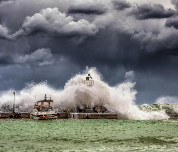 Storm waves crash on tied up boats with storm clouds.