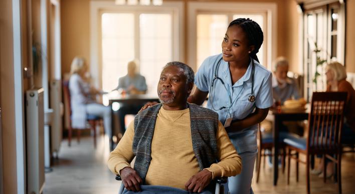 An African American man being pushed in a wheel chair by an African American nurse.